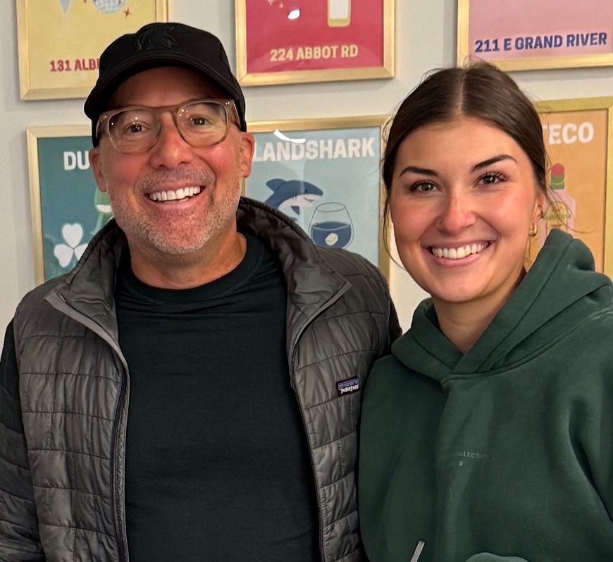 Dave Knoepfle and his daughter Ellie, smiling, in front of a wall of framed posters.