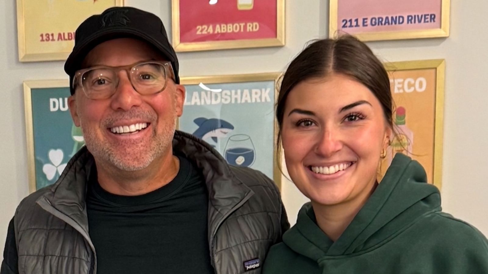 Dave Knoepfle and his daughter Ellie, smiling, in front of a wall of framed posters.